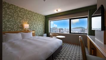 Habitación de hotel con cama, escritorio, silla, mesita y ventana con vista a la ciudad.