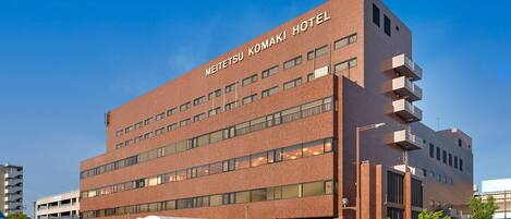 A modern hotel building with multiple floors, large windows, and a prominent sign reading "METAFITETSU KOMAKI HOTEL".