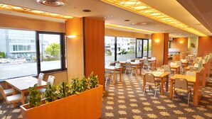 A hotel lobby with a carpeted floor, wooden tables and chairs, large windows, and a plant display. - Meitetsu Komaki Hotel (Komaki)