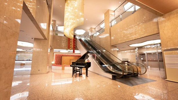 A modern lobby with a grand piano, an escalator, and a reception desk. - Meitetsu Komaki Hotel (Komaki)
