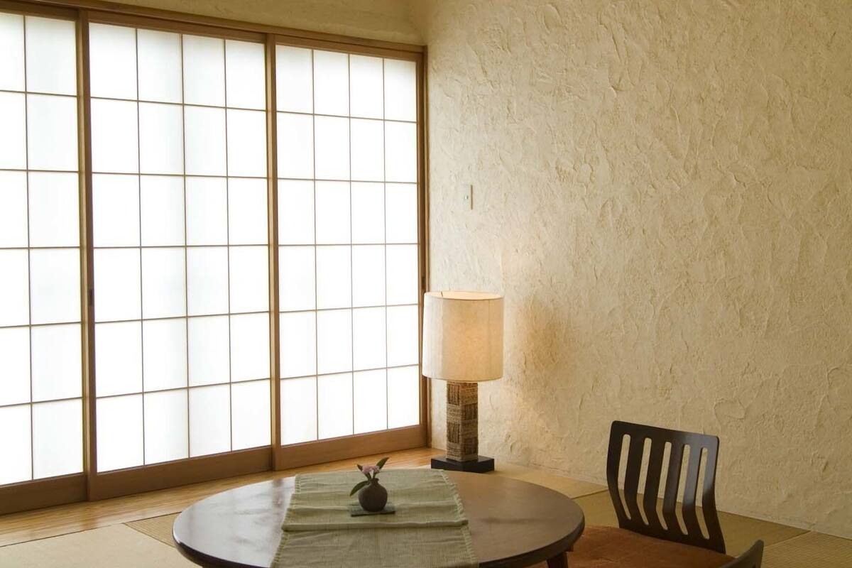 A traditional Japanese room with tatami flooring, a low table with cushions, a paper lantern, and a sliding shoji screen.