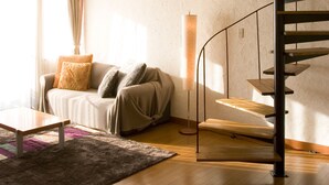 A modern living room with a wooden floor, a sofa with cushions, a coffee table, and a spiral staircase. - Hotel&Resort Mashio (Oshima)