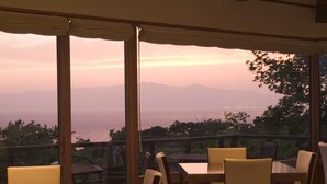 A terrace with tables and chairs, overlooking a scenic view of the sea and mountains. - Hotel&Resort Mashio (Oshima)