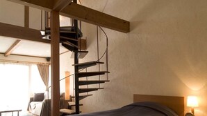 A bedroom with two beds, wooden beams, a spiral staircase, a bedside table with a lamp, and a view of a balcony. - Hotel&Resort Mashio (Oshima)