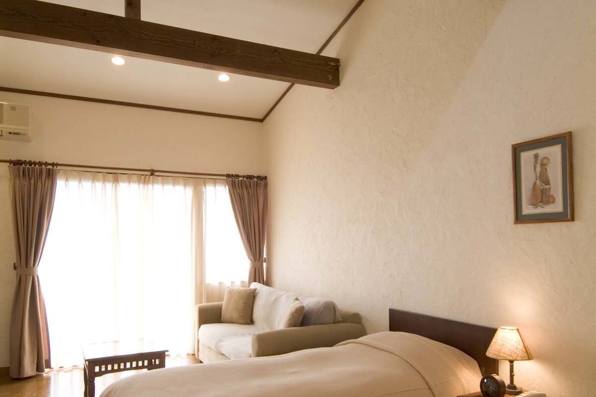 A hotel room with two beds, a ceiling fan, a bedside lamp, and a window with curtains.