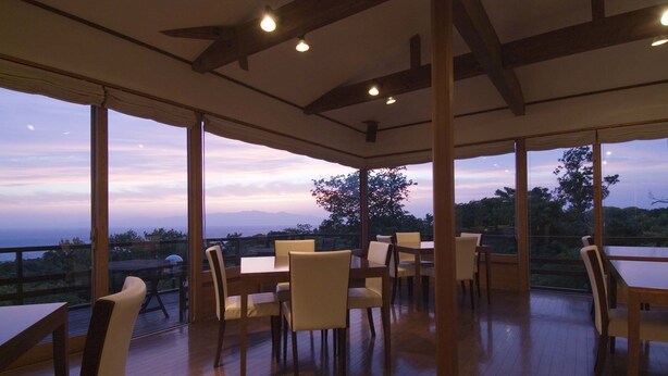 An open-plan dining area with wooden flooring and large windows offering a view of the outdoors. - Hotel&Resort Mashio (Oshima)