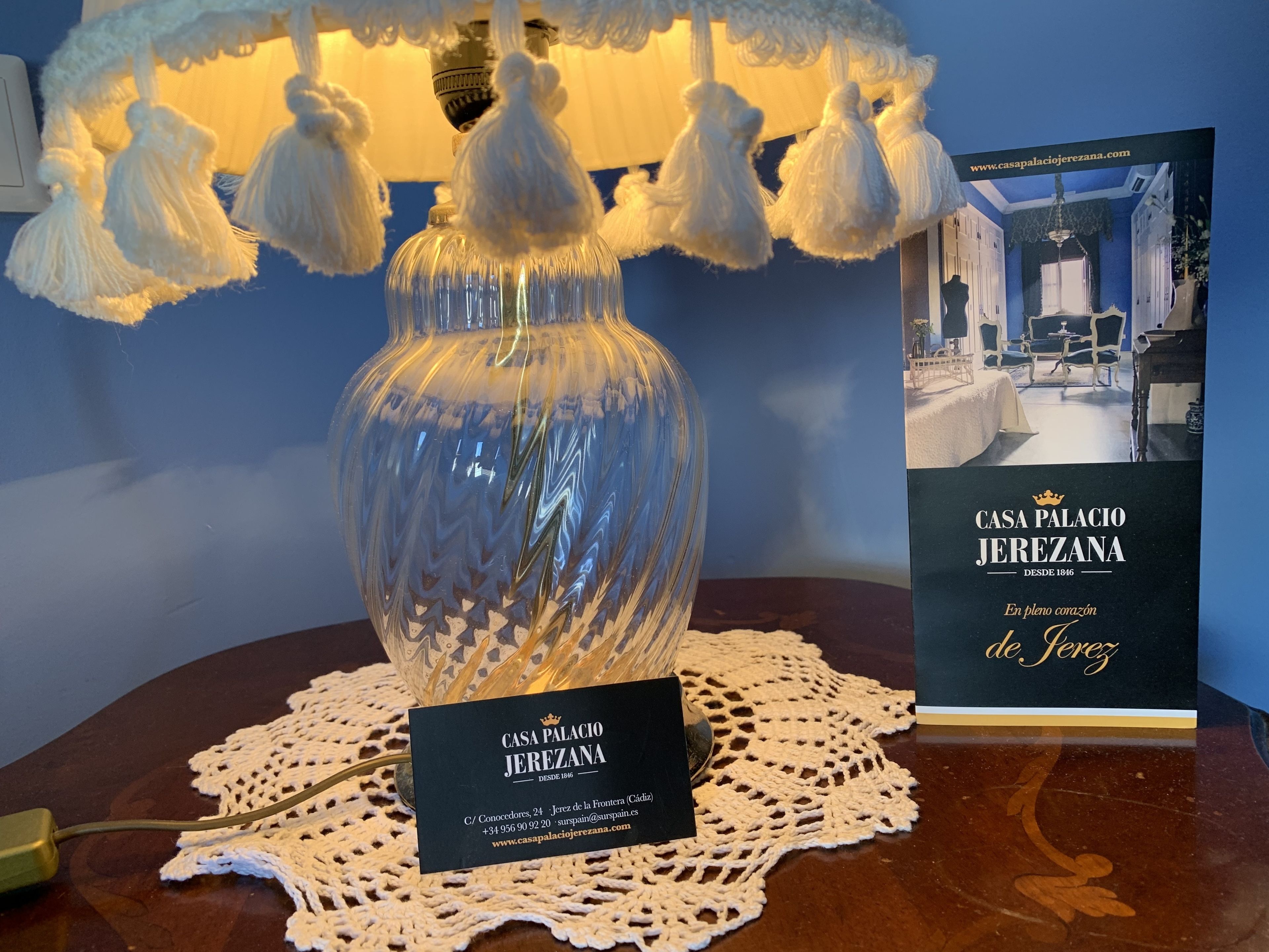 A clear glass vase with a textured pattern, a lace doily, and a business card for Casa Palacio Jerezana.