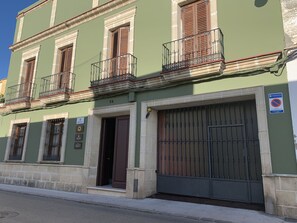 Un edificio con fachada verde, varias ventanas con contraventanas y un gran portón metálico.