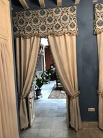 Un pasillo con cortinas color beige, suelo de baldosas y una planta en maceta.