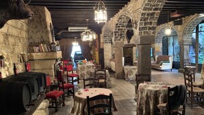 An indoor dining area with stone walls, wooden tables, and chairs. There are bookshelves and a fireplace.