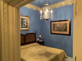 A bedroom with a bed, a chandelier, and two framed pictures on the wall.