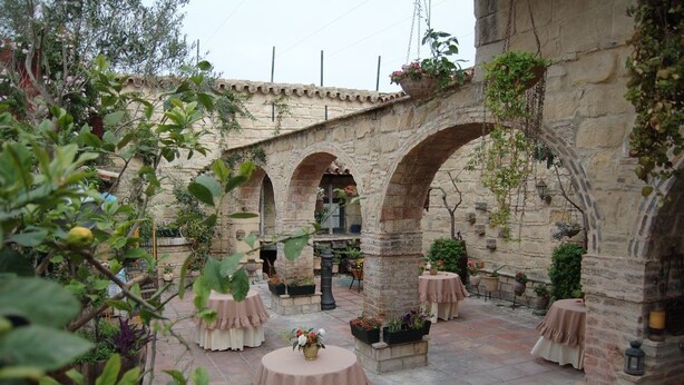 An outdoor patio area with stone arches, round tables with pink tablecloths, and potted plants.