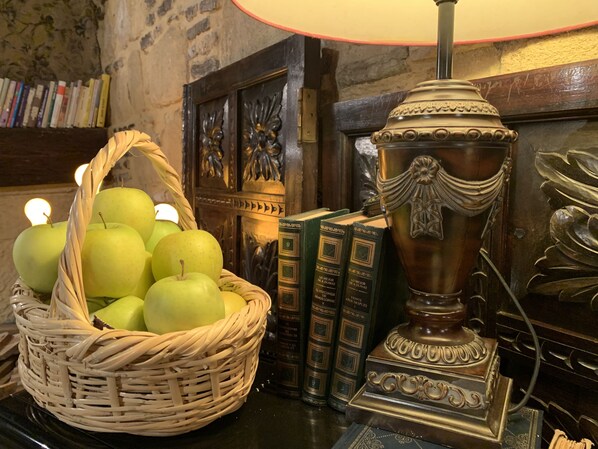 Um quarto com uma cesta de vime cheia de maçãs verdes, um braseiro de latão e uma fileira de livros em uma estante.