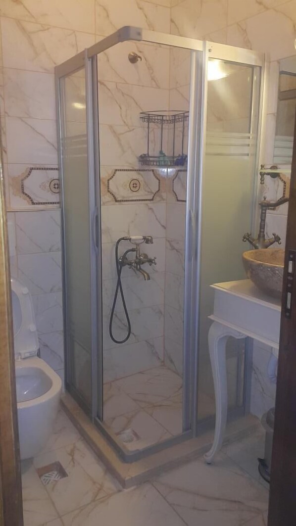 A bathroom with a glass-enclosed shower, a marble-tiled floor, a white toilet, and a sink with a stone basin. - Aristonicus Boutique Hotel (Bergama)