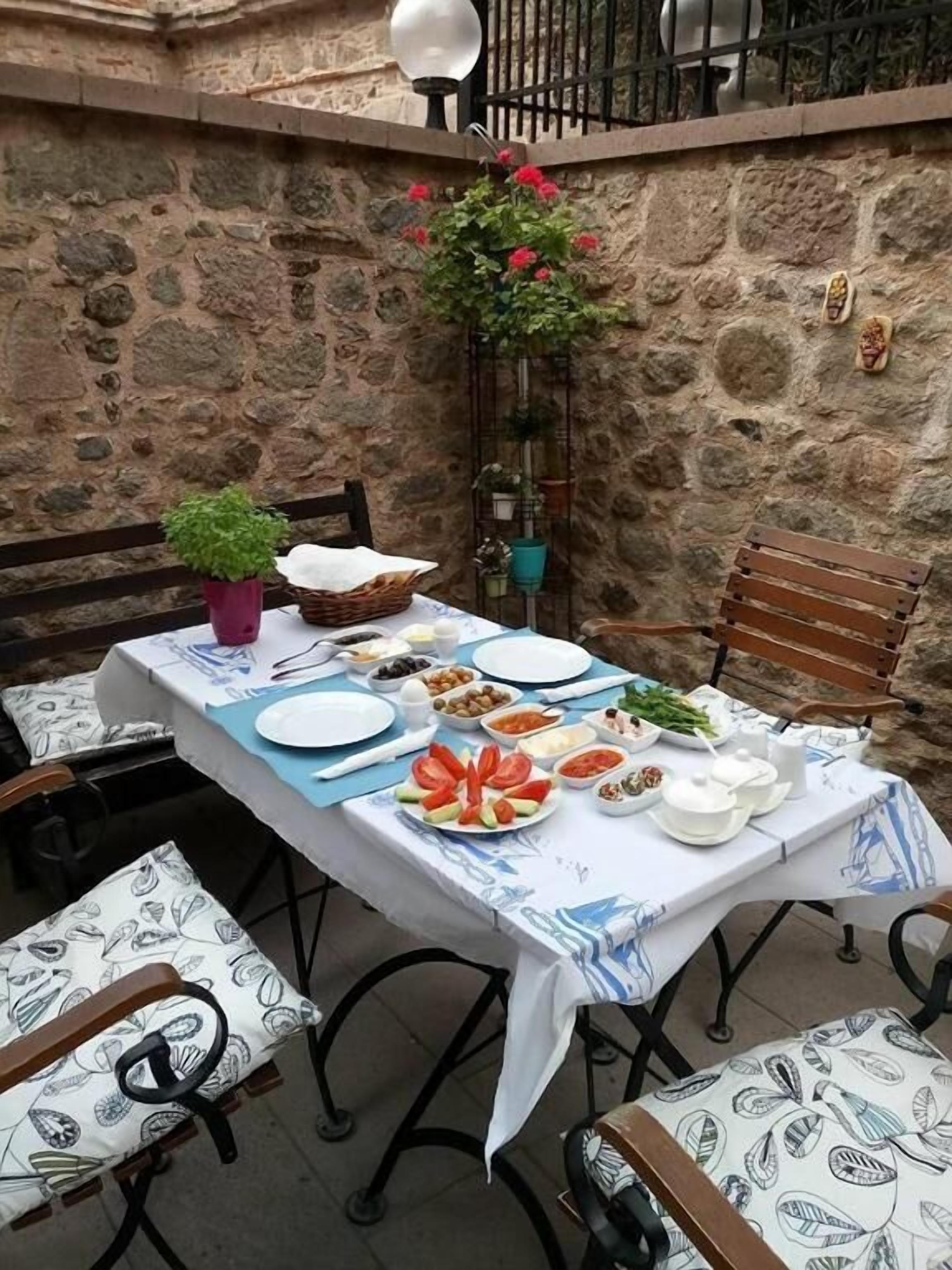 Un espacio de comedor al aire libre con paredes de piedra, una mesa dispuesta con platos, tazones y una planta en maceta.