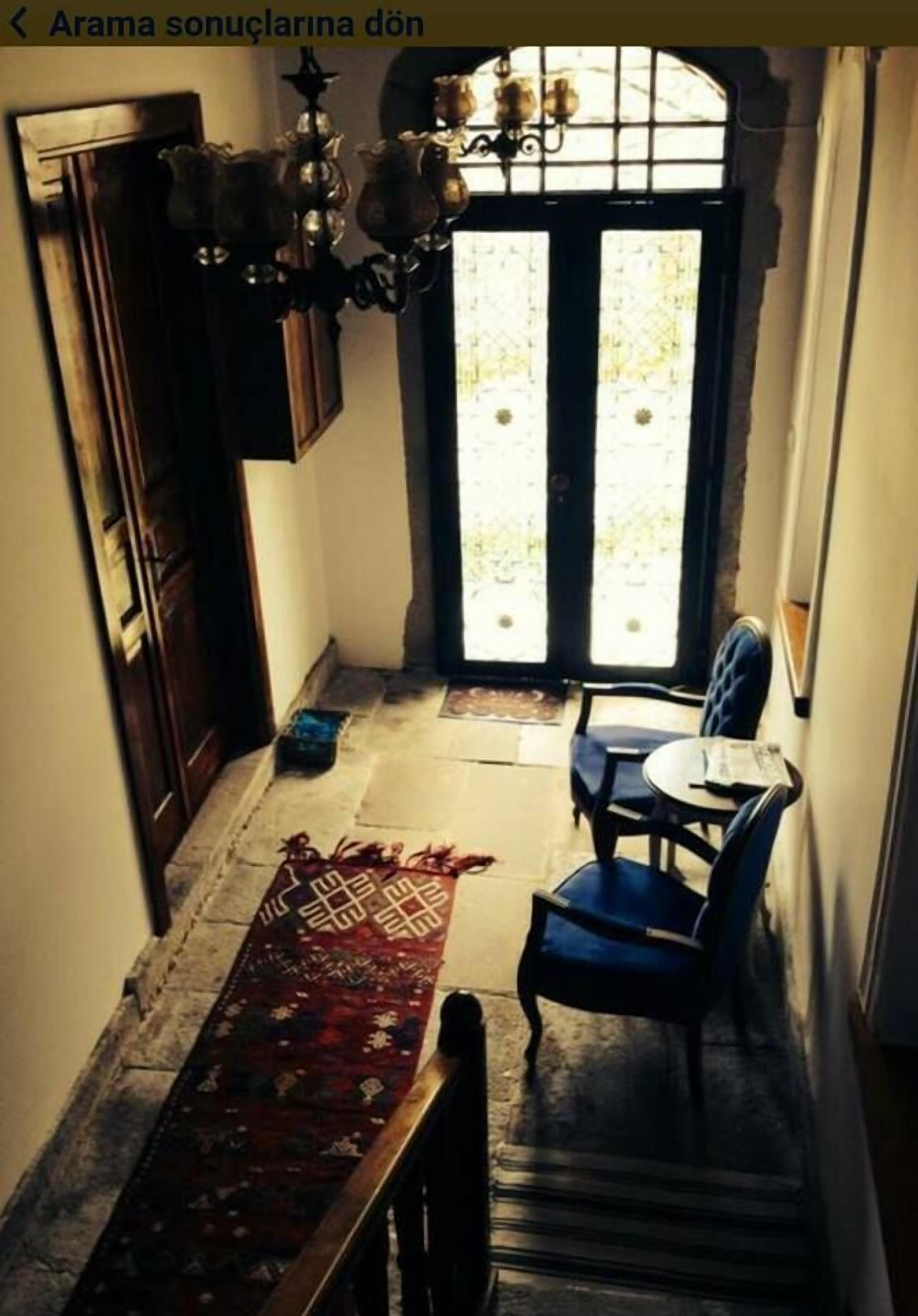 A narrow hallway with a wooden door, a chandelier, a patterned rug, a blue chair, and a small table.