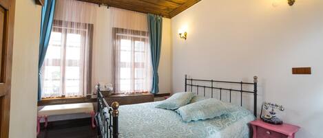 A bedroom with a bed, a bench, a nightstand, and a window with curtains.