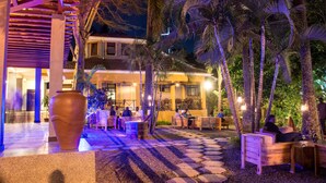 An outdoor seating area with tables and chairs, surrounded by palm trees and a large decorative vase. - Meley Impala Hotel (Kampala)