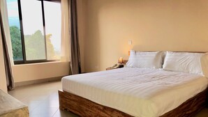 A neatly made bed with white linens in a room with a large window, a bedside table with a lamp, and a telephone. - Meley Impala Hotel (Kampala)