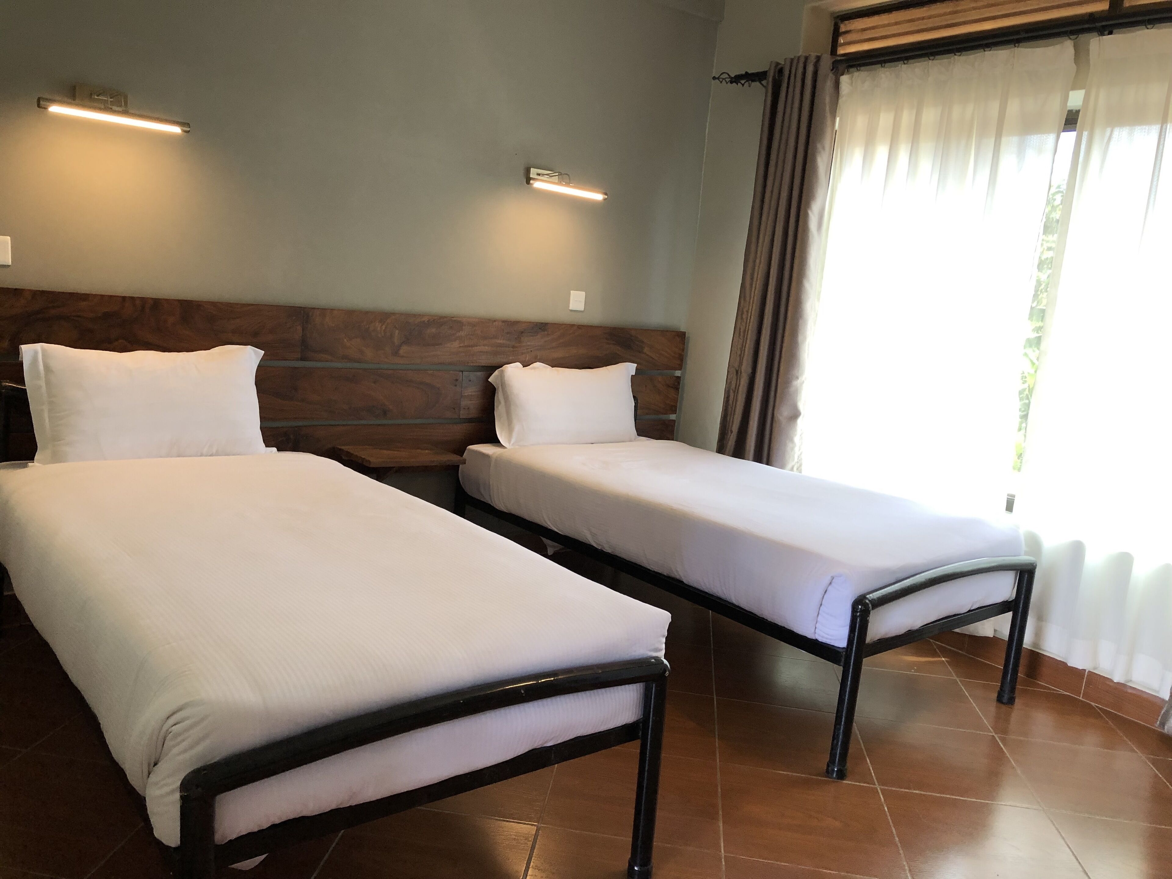 Two single beds with wooden headboards, a tiled floor, and a window with curtains.