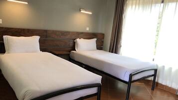 Two single beds with wooden headboards, a tiled floor, and a window with curtains.