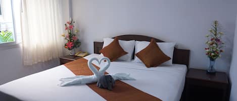 Una cama bien hecha con una toalla con forma de corazón y un diseño de toalla con forma de cisne, cabecera de madera, almohadas blancas y almohadas decorativas marrones.