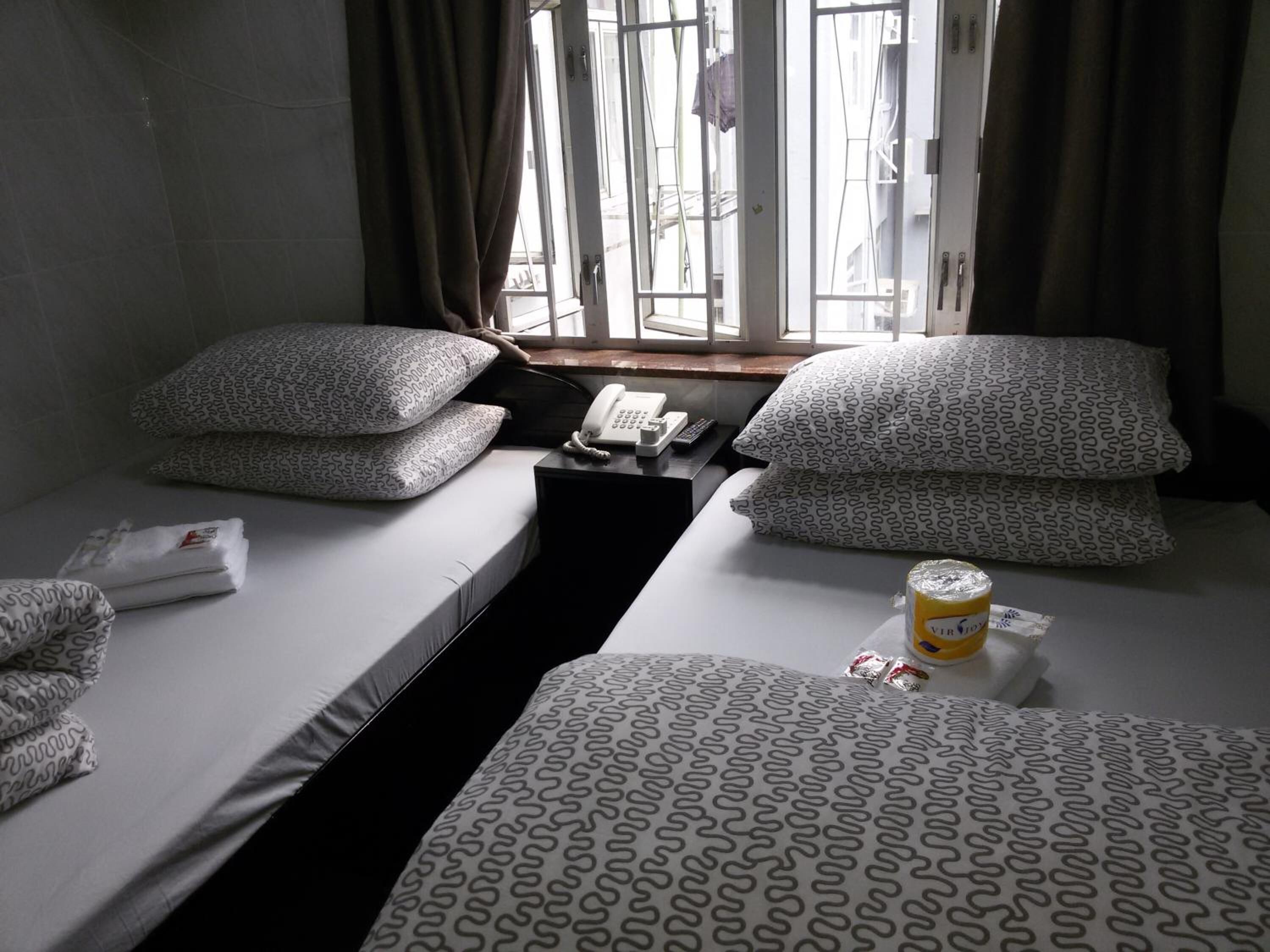 A hotel room with two single beds, each with patterned bedding and pillows. There is a small table with a telephone and a cup of coffee.