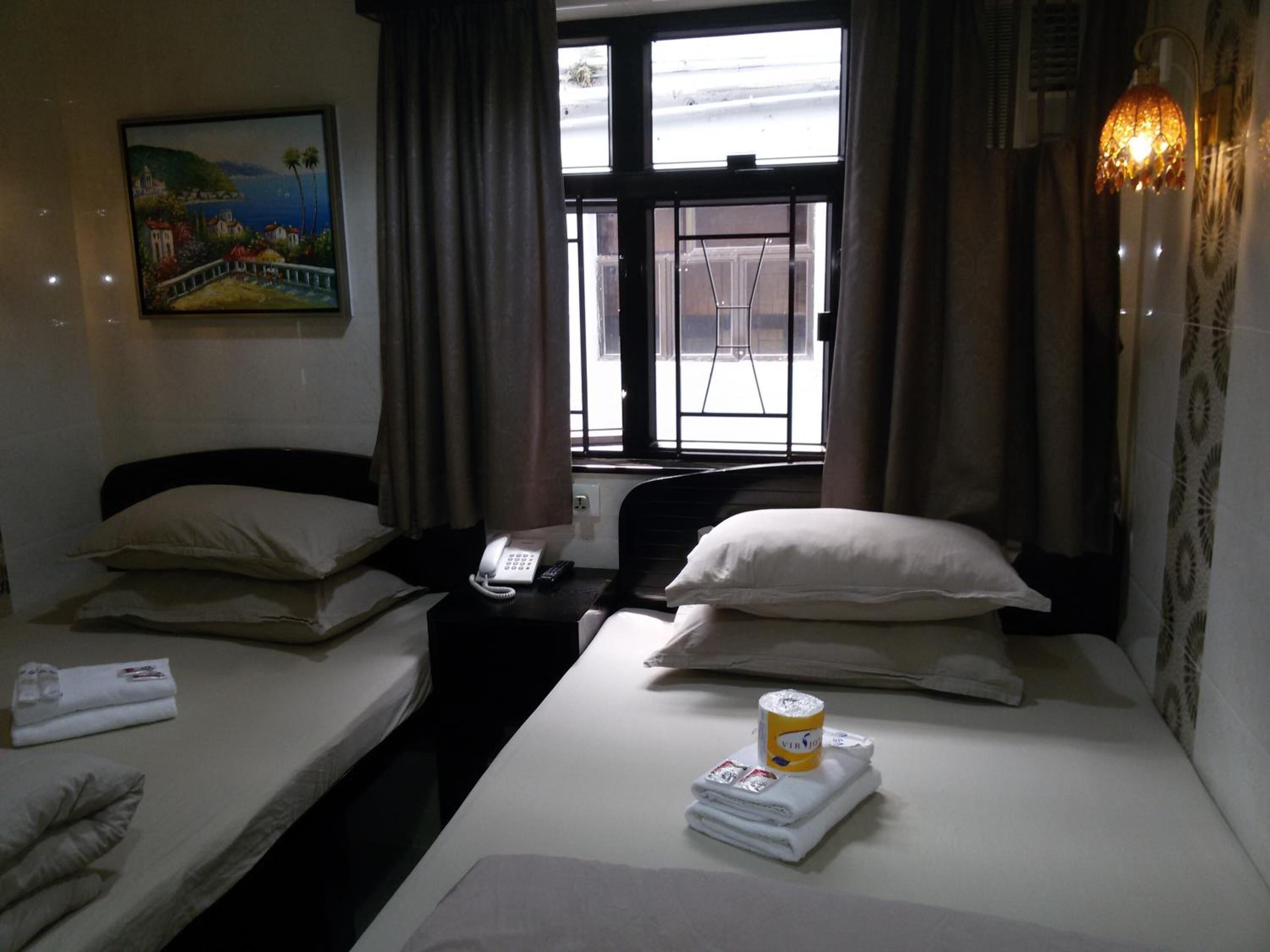 A hotel room with two beds, a painting on the wall, a telephone on the nightstand, and a window with curtains.