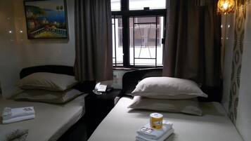 A hotel room with two beds, a painting on the wall, a telephone on the nightstand, and a window with curtains.