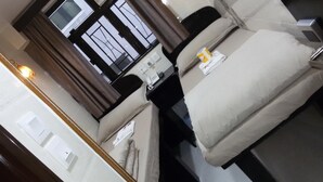 A hotel room with a bed, a bedside table, a lamp, a window with curtains, and a view of the outside. - Tom's Guest House (Kowloon)