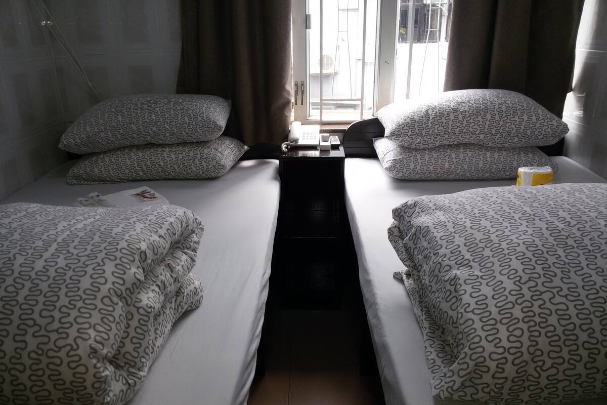 A twin room with two beds, each with patterned bedding and pillows. There is a small table with a telephone and a cup.