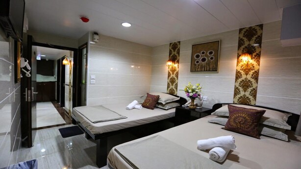 A hotel room with two beds, a bedside table with a lamp, a wall-mounted air conditioner, and a bathroom visible through an open door. - Tom's Guest House (Kowloon)