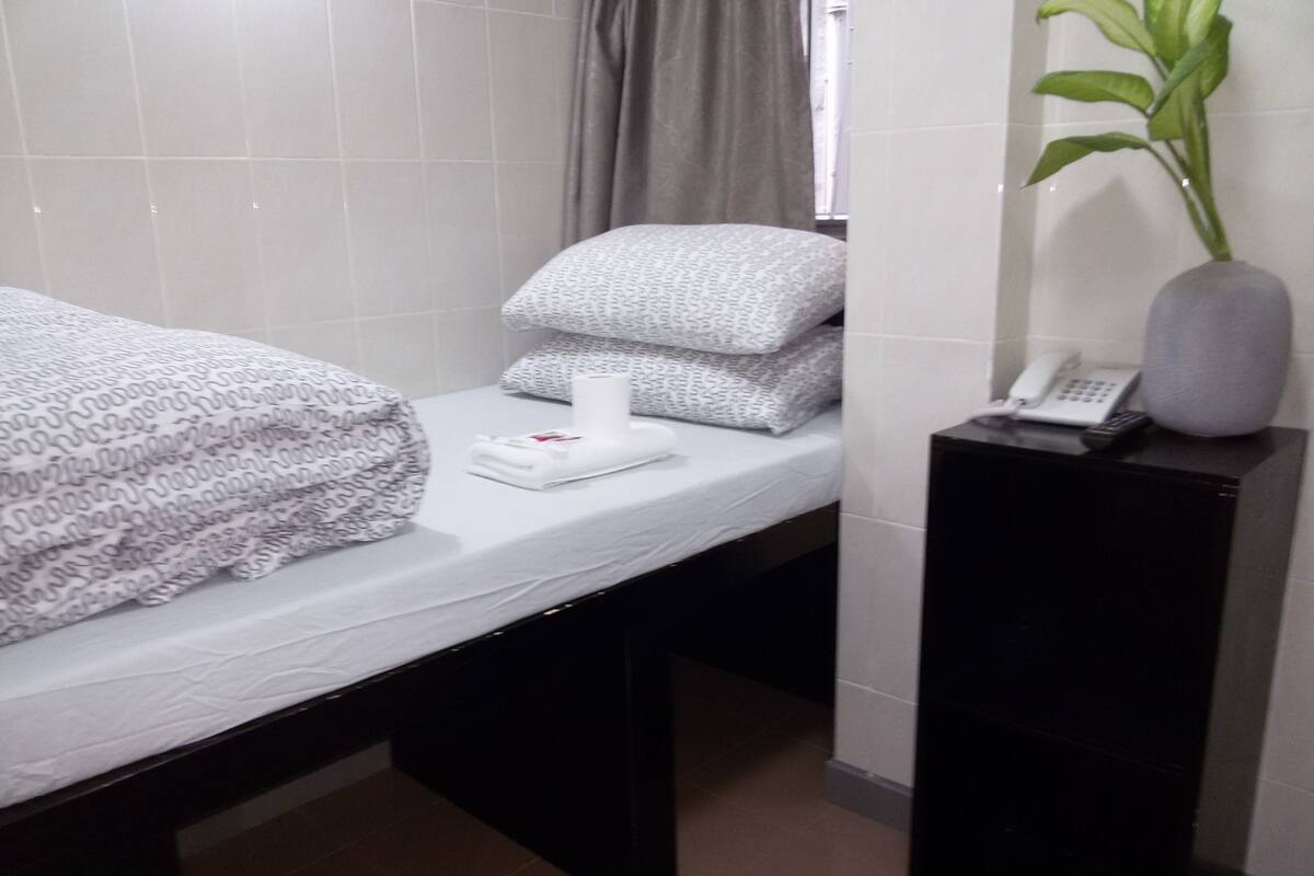 A hotel room with a bed, a bedside table with a phone and a vase, and a window with curtains.