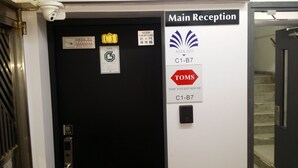 A hotel reception area with a black door, a fire safety sign, and a sign for Tom's Guest House. - Tom's Guest House (Kowloon)