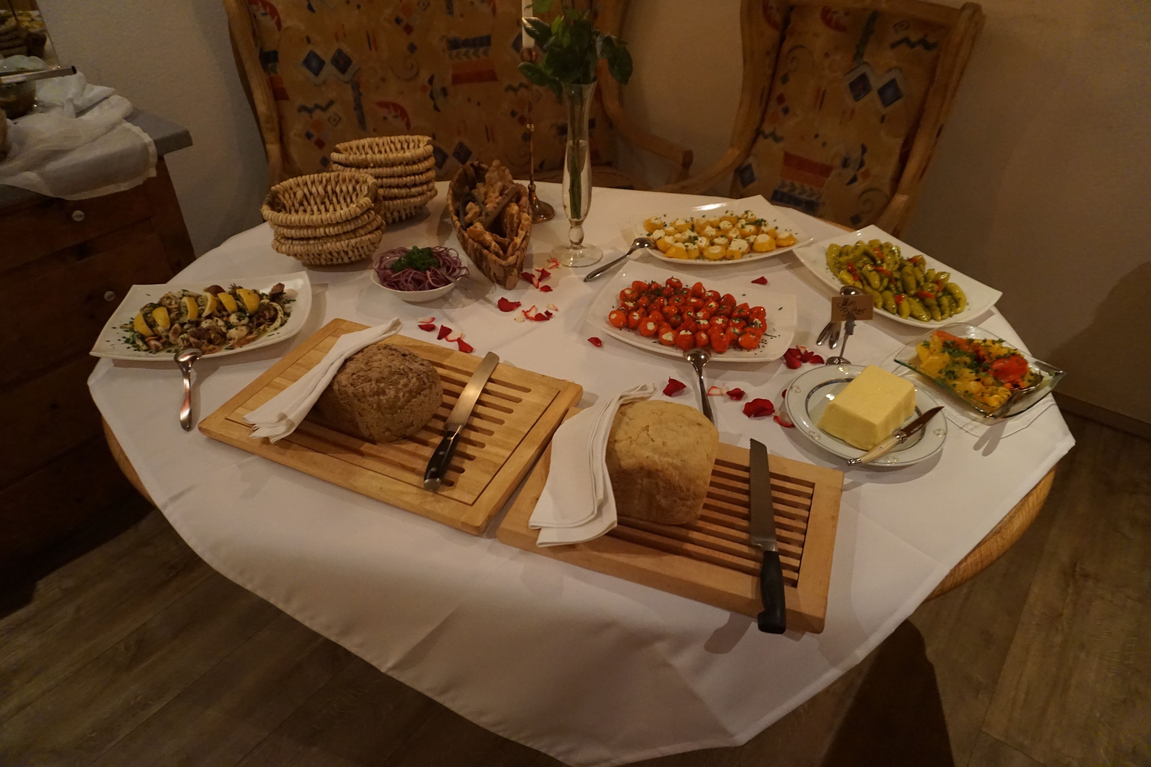 Ein Tisch ist reichhaltig gedeckt mit verschiedenen Speisen, darunter Brot, Käse und Gemüse, sowie einem Messer und Löffel.
