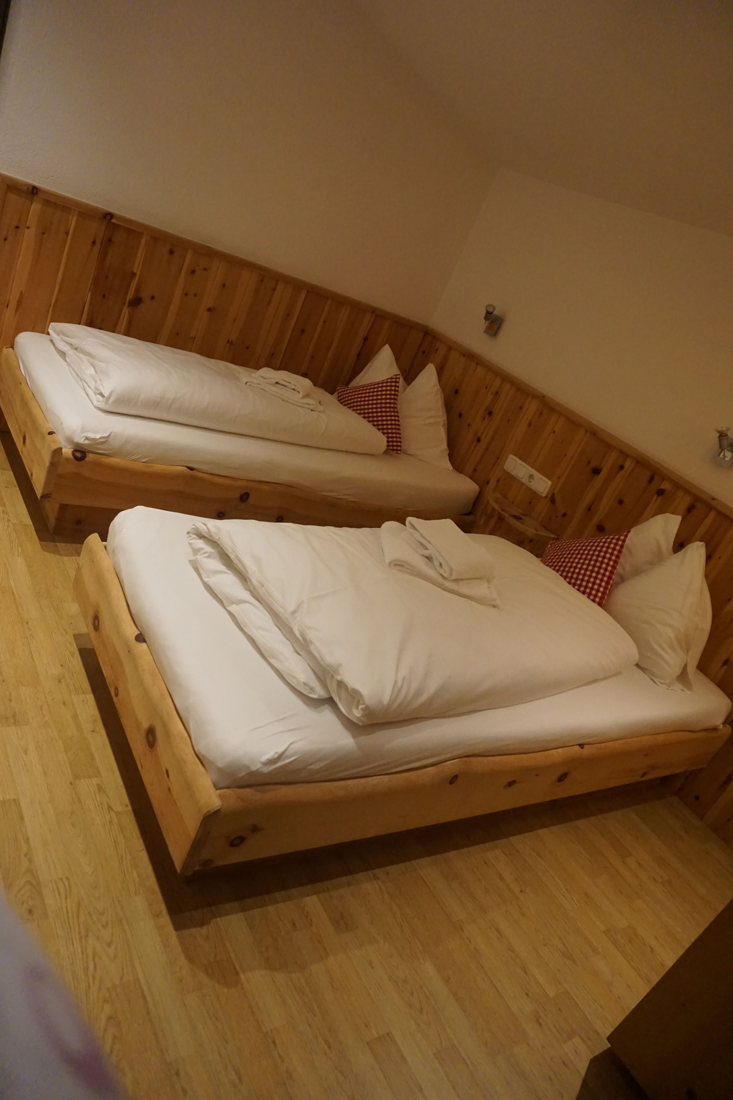 Zwei Holzbetten mit weißer Bettwäsche und roten Kissen mit Schachmuster in einem Raum mit Holzwänden und Holzböden.