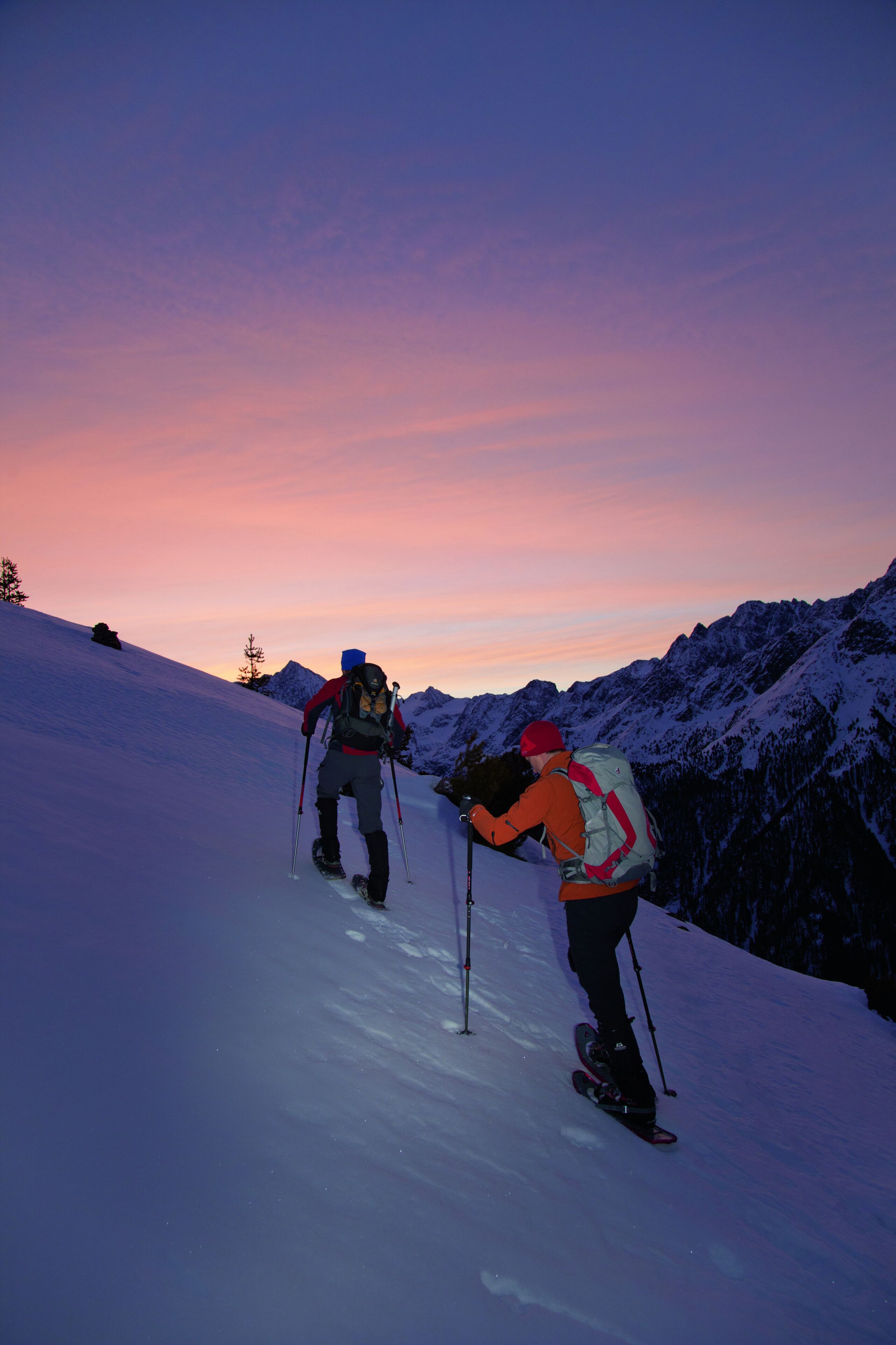 Two people skiing on a snowy mountain slope during sunset.