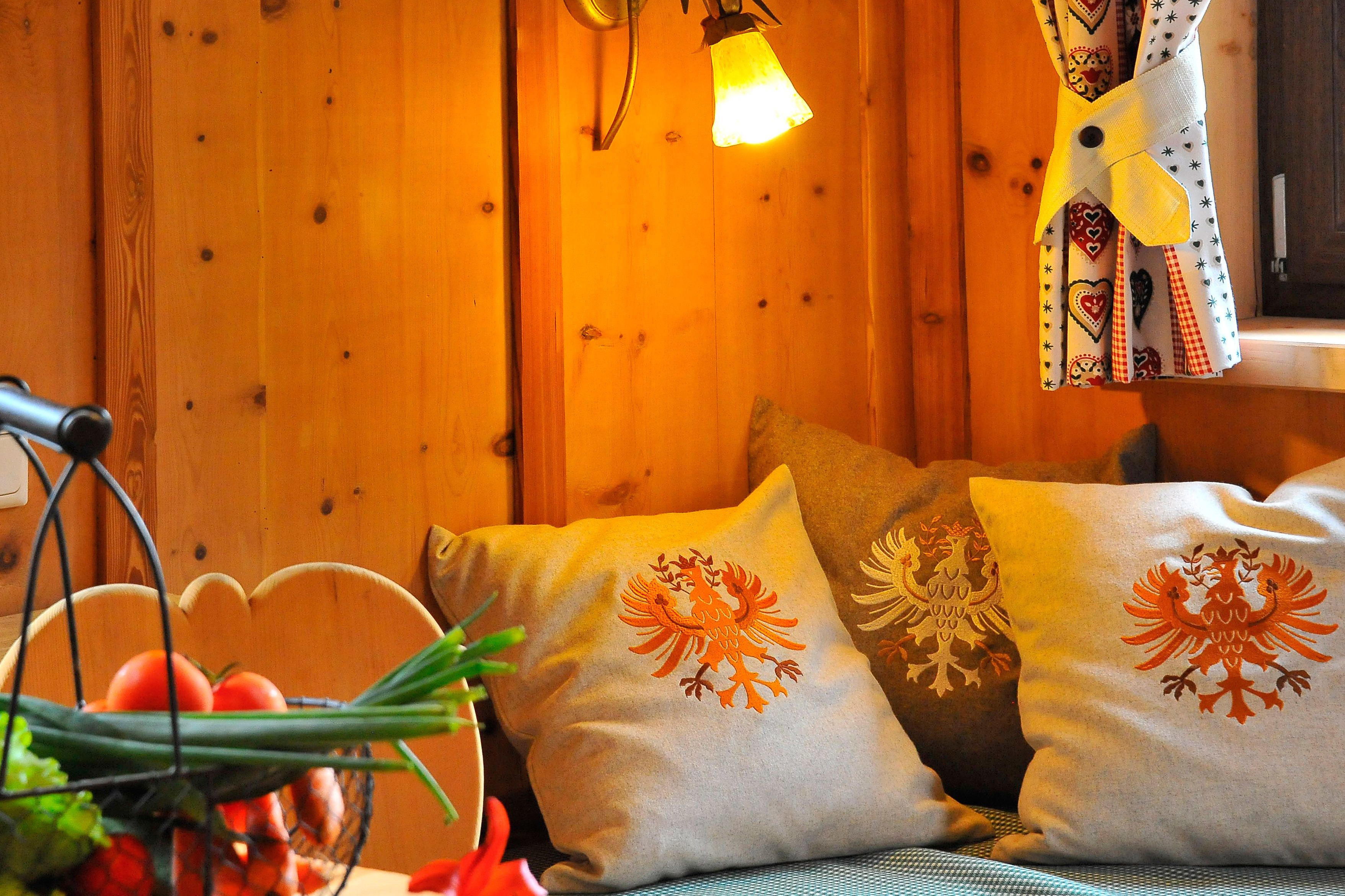 Une pièce chaleureuse aux murs en bois, agrémentée d’un luminaire suspendu et de coussins décoratifs ornés de motifs d’oiseaux.