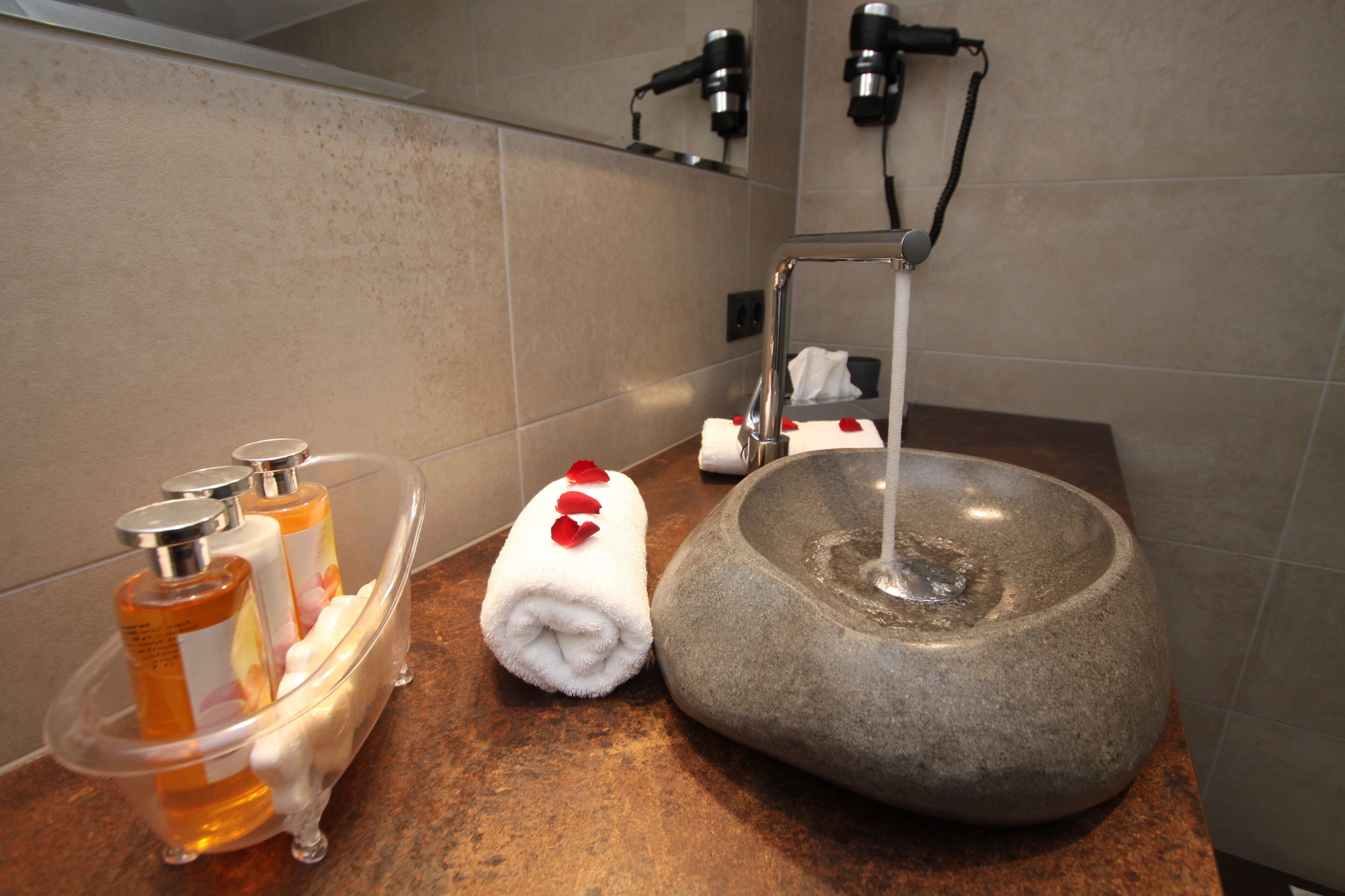 A bathroom with a stone sink, a glass soap dispenser, and a towel with rose petals.