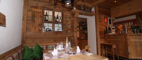 A wooden interior with a dining table set for four, a bar area, and a wooden bench with green cushions.