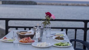 Uma mesa posta para refeição com diversos pratos, um vaso com flores e vista para o mar.