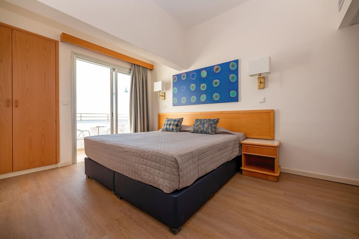 A bedroom with a large bed, wooden wardrobe, and a view of the balcony.
