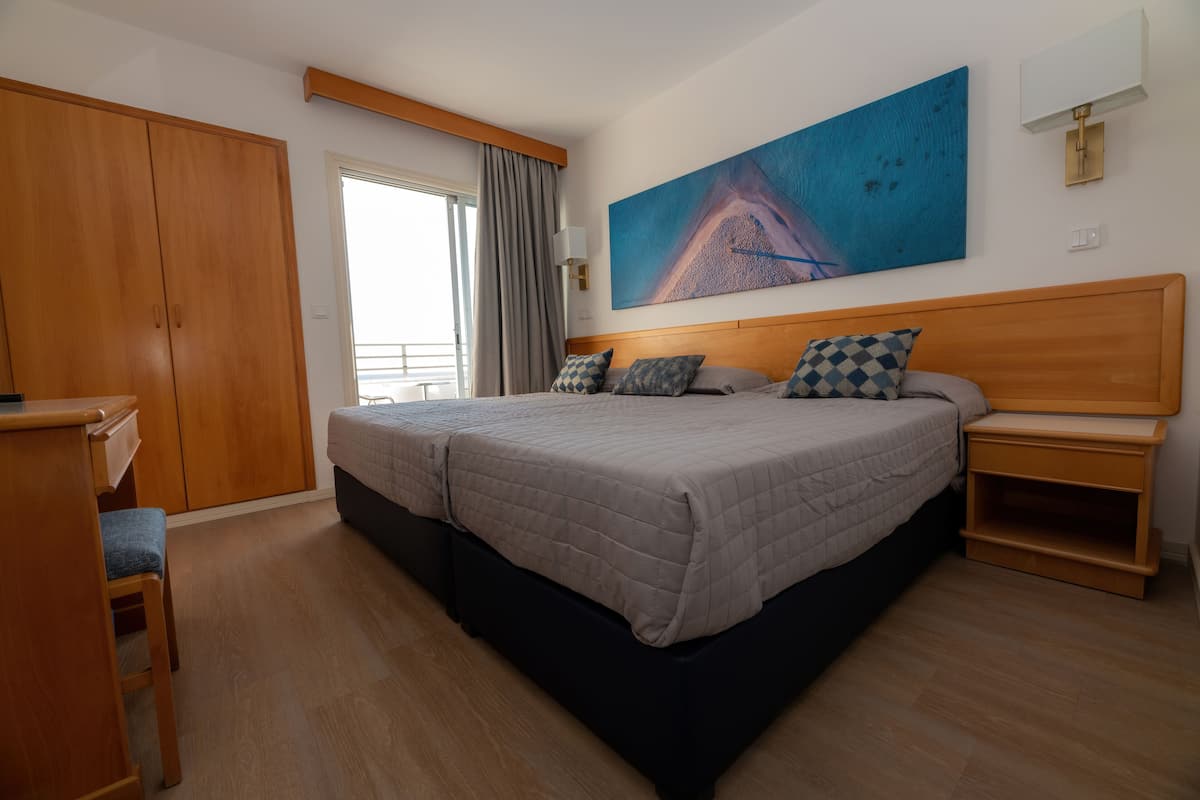 A bedroom with a large bed, wooden wardrobe, and a painting on the wall.