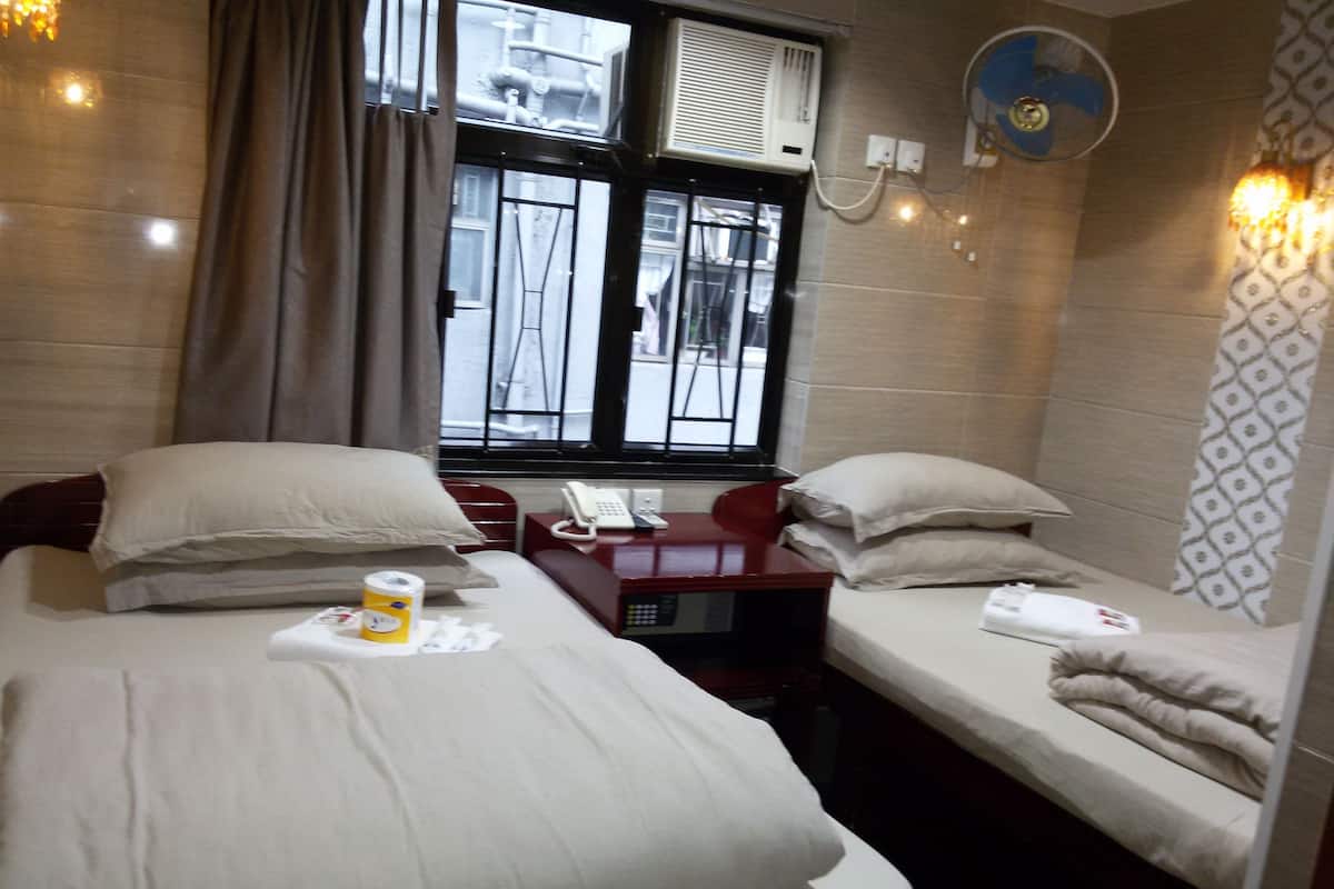 A hotel room with two beds, a desk with a telephone, and a window with blinds.