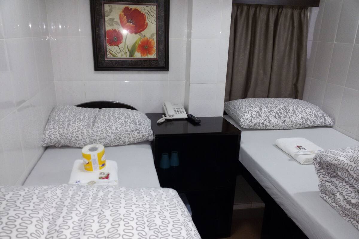 A hotel room with two single beds, a small table with a phone, a yellow cup, and a framed picture on the wall.