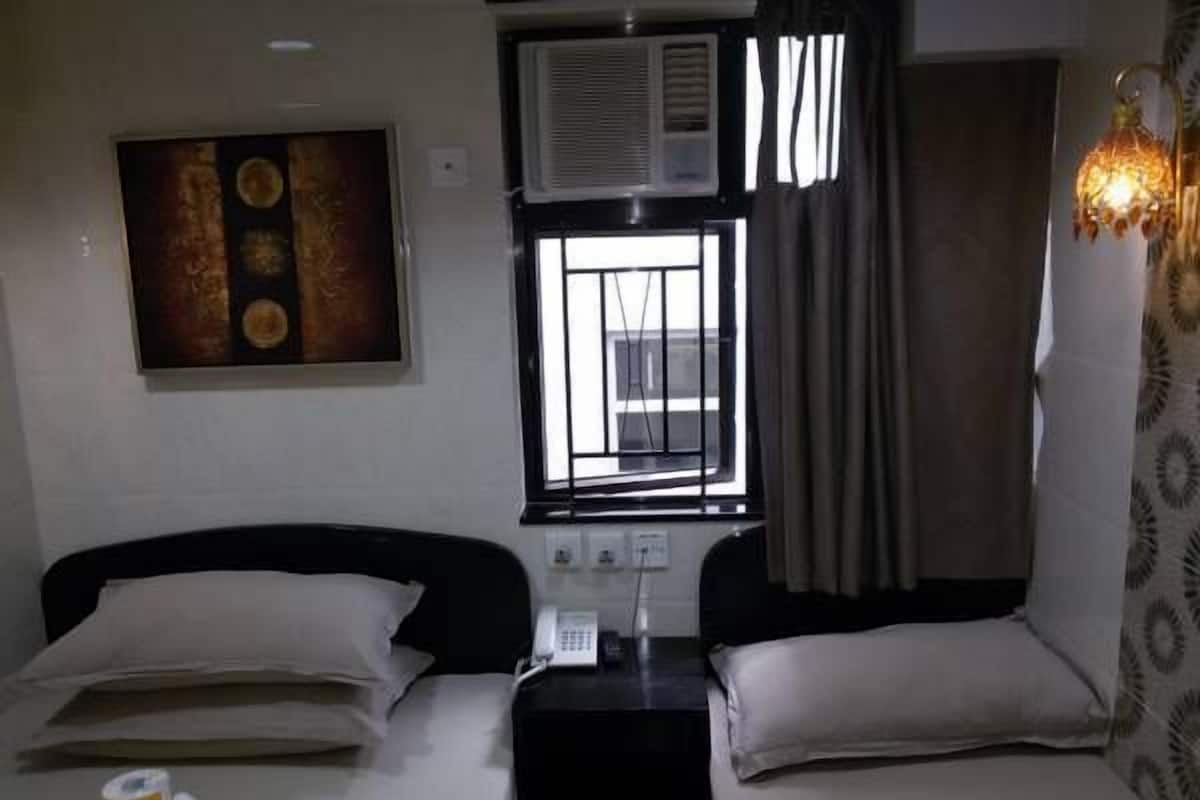 A hotel room with two beds, a painting on the wall, an air conditioning unit, a telephone, and a patterned curtain.
