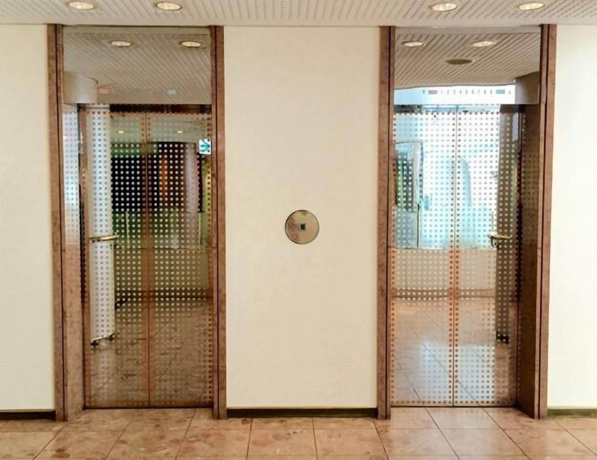 A set of double doors with a perforated pattern, a round metallic plate, and a tiled floor.