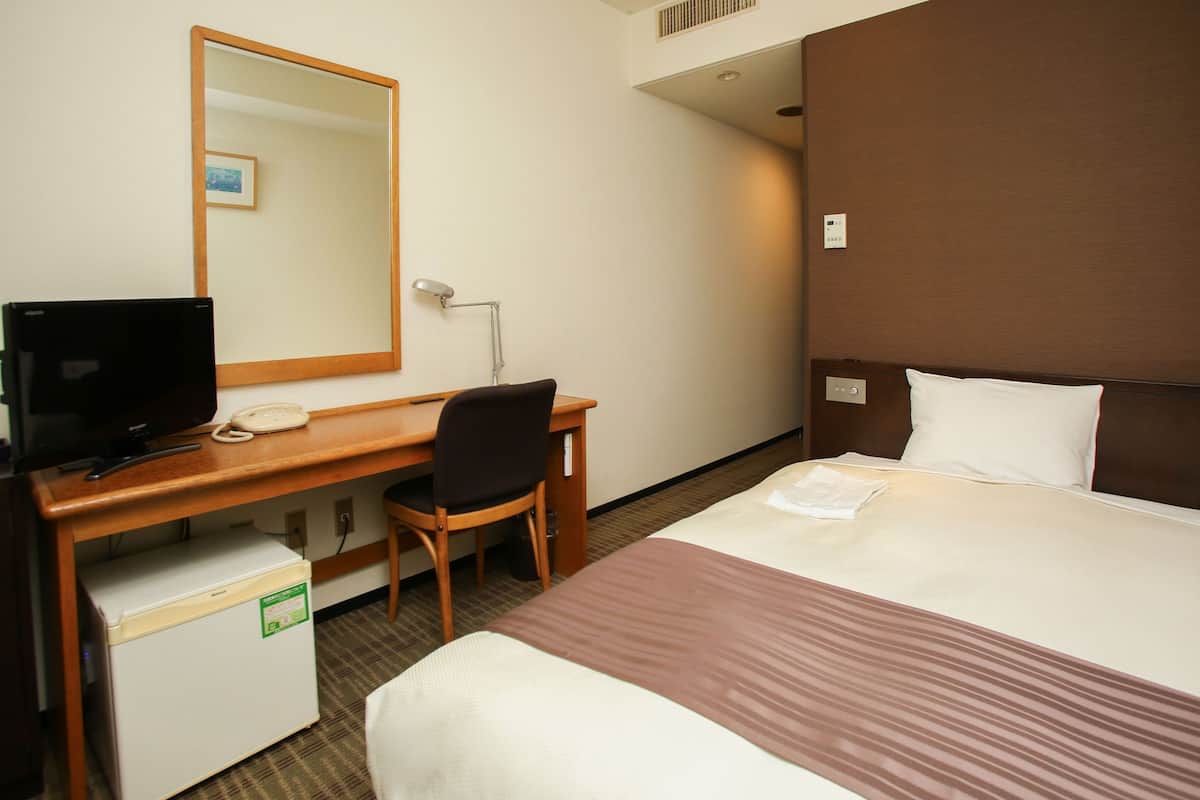 Een hotelkamer met een bed, een bureau met een computer, een stoel en een kleine koelkast.