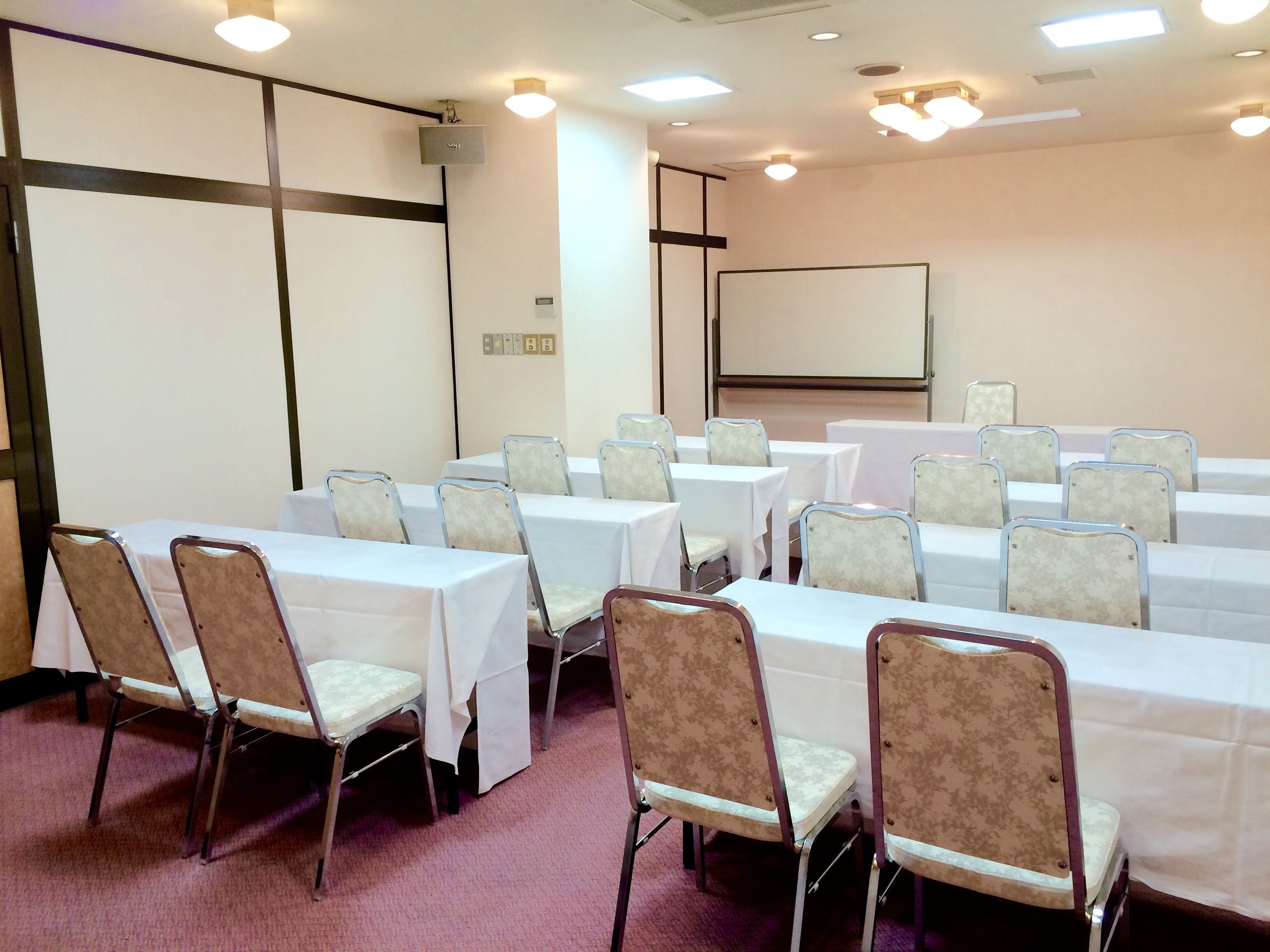 Una sala de conferencias con mesas y sillas, una pantalla de proyector y luces en el techo.