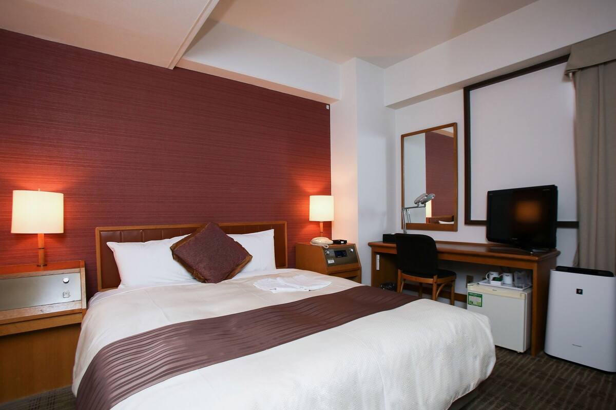 Hotelkamer met een groot bed, twee bedlampen, een bureau met stoel, een televisie en een minibar.
